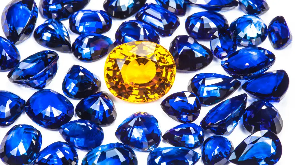 Faceted blue sapphires with a central yellow gemstone on a white background, image for gemstone analysis.