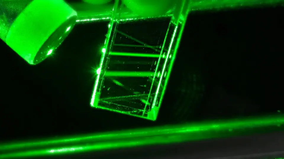 Raman setup with intense green laser focused on a transparent sample, reflecting light beams.